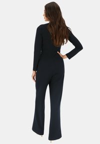 Granatowy kombinezon z długimi rękawami, dopasowanym gorsetem i szerokimi nogawkami. Gładki materiał o minimalnych detalach i subtelnym szwie z tyłu.