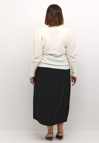 Witte, gestructureerde trui met opgeblazen schouders, gecombineerd met een zwarte, lange rok. De outfit heeft een getailleerd ontwerp en een gladde afwerking.