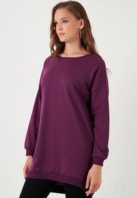 Felpa lunga viola con maniche lunghe e vestibilità comoda, spalle scese e polsini a coste; tessuto morbido e dettaglio dell'orlo posteriore allungato.