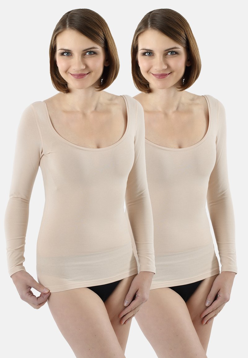 Nude long-sleeve fitted top with a scoop neckline and smooth texture. Model adjusts the hem over black bottom wear. Two identical views.