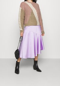 Strickpullover in Beige, Rosa und Creme mit geometrischen Mustern; lavendelfarbenen Satin-Midikleid; schwarze Knöchelstiefel; kleine schwarze Handtasche.