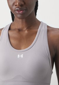 Scollo sportivo grigio chiaro con una texture liscia, design a spalle scoperte e un logo bianco nella zona del petto. Presenta dettagli a coste lungo l'orlo.