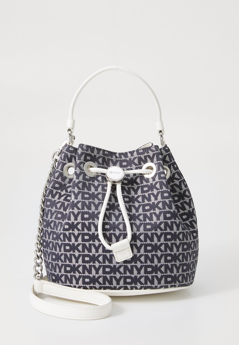 Bucketveske i marineblå tekstil med hvitt logo-mønster. Har et hvitt håndtak på toppen, snøring til lukking og sølvkjede skulderstropp.
