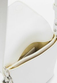Biała skórzana torebka crossbody o gładkiej fakturze, z widocznym przeszyciem i jedną komorą z beżowym wykończeniem wewnątrz.
