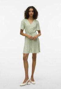 Robe vert clair avec un décolleté en V, de courtes manches bouffantes, une fermeture à boutons, une ceinture à la taille et de petits motifs floraux sur l'ensemble.