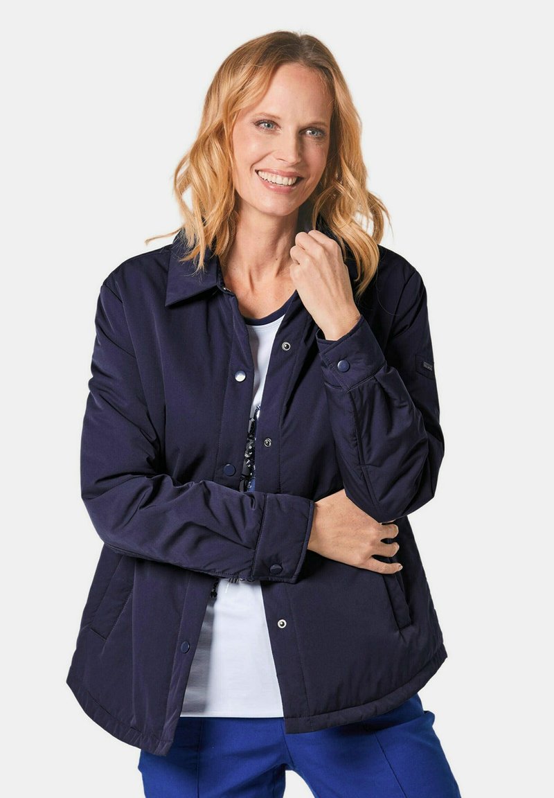 Marineblaue, gepolsterte Jacke mit Knopfverschluss vorne, Kragen und Seitentaschen. Der Stoff ist glatt mit einer matten Oberfläche.