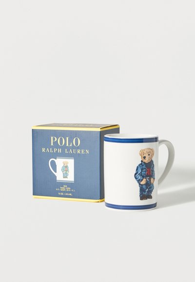 Λευκή κεραμική κούπα με μπλε περίγραμμα, με αρκούδα ντυμένη με τζιν, που στέκεται δίπλα σε μια μπλε κουτί Polo Ralph Lauren.