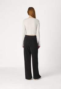 Top court blanc avec texture côtelée et ourlet brut ; associé à un pantalon à jambes larges plissé noir avec taille élastique.