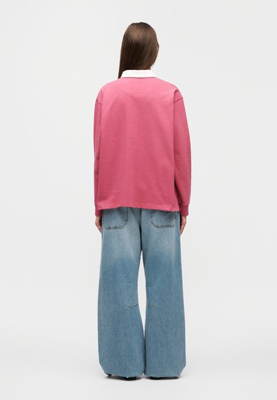 Ροζ φούτερ με λευκή γιακά, άνετη γραμμή και πλευρικές σχισμές. Συνδυάζεται με φαρδιά τζιν παντελόνια ανοιχτό μπλε χρώμα με πίσω τσέπες και ξεθωριασμένο φινίρισμα.
