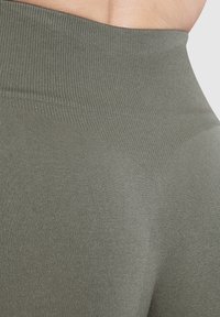 Leggings a vita alta in verde oliva, realizzati in tessuto a coste elasticizzato con un design aderente e una texture liscia. Senza cuciture visibili.