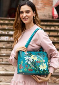 Teal leren handtas met bloemenborduurwerk in wit en rood, met een ruime indeling en een schouderband. Accenten in goudkleurig beslag.