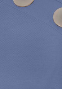 Tela texturizada azul con dos grandes botones brillantes hechos de un material de color claro, ubicados en la costura del hombro.