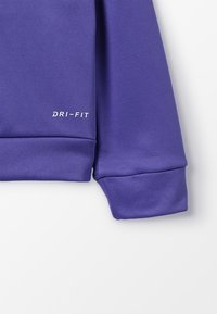 Fioletowa koszulka z długim rękawem DRI-FIT z gładkiego, teksturowanego materiału; na mankiecie rękawa znajduje się detal z logo w kolorze białym.