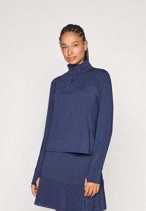 Haut à manches longues marine avec un col haut, fermeture éclair semi-ouverte et un motif texturé sur le devant. Manches longues avec ouverture pour les pouces et coupe décontractée.