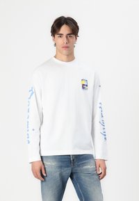 Tricou alb cu mâneci lungi, având un grafic albastru pe mâneca stângă și o imprimeu colorat pe piept. Material din bumbac moale, croi relaxat.