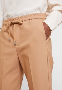 Beige skräddarsydda byxor med elastisk midja, dragsko och sidofickor. Slät tyg med mjuk textur och rak bendesign.