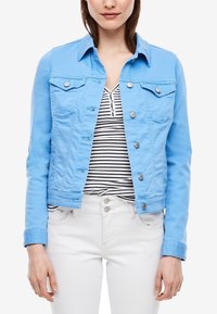 Hellblaue Denimjacke mit Vordertaschen, silbernen Beschlägen, Knopfverschluss und tailliertem Schnitt, getragen über einem gestreiften Oberteil.