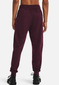 Bordeauxfarbene Jogginghose mit elastischem Bund, schmal zulaufenden Beinen und einer Gesäßtasche. Weicher Stoff mit glatter Textur und Kordelzugabschlüssen.