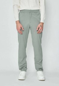Jogging slim fit en gris clair, avec une taille élastique, des poches frontales et une texture lisse. Associé à des baskets blanches.