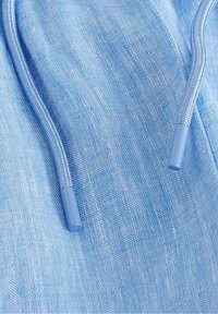 Jasnoniebieska tkanina o fakturowanym splocie, wyposażona w jasnoniebieski sznurek z plastikowymi zakończeniami. Materiał wydaje się miękki i przewiewny.