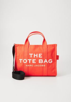 Geantă de pânză roșie cu text alb care spune „GEANTA TOTE” și „MARC JACOBS.” Prezintă mânere scurte și o curea de umăr neagră detașabilă.