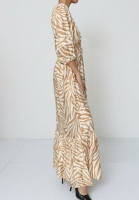 Robe maxi à motif zèbre beige et blanc. Manches bouffantes avec des poignets élastiques, ceinture à la taille et ourlet froncé. Texture de tissu lisse.