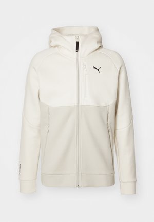 Lys beige zip-hoodie med hætte, designet med cremefarvede paneler, høj krave, to lynlåslommer og et sort logo på brystet.