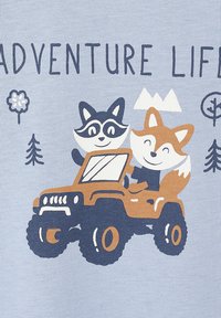 Der graue Stoff zeigt eine verspielte Illustration eines Waschbären und eines Fuchses in einem braunen Jeep, umgeben von Bäumen und Bergen, mit dem Text "ABENTEUER LEBEN".