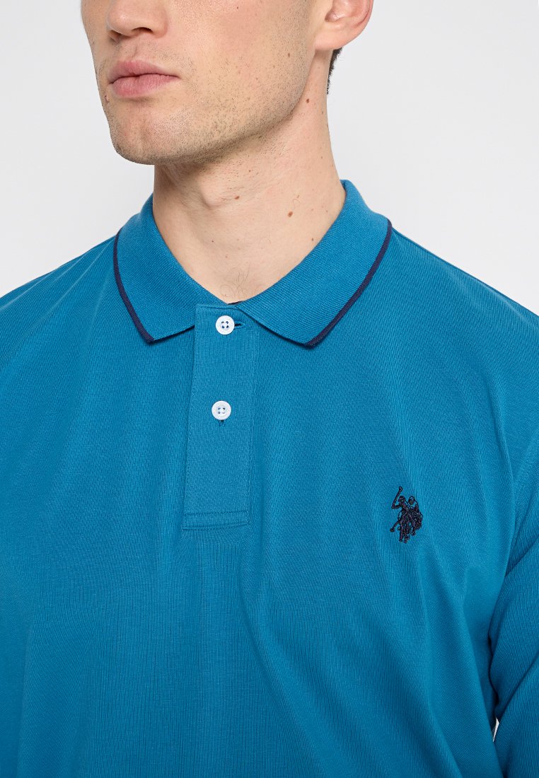 Polo shirt turchese con texture a coste, colletto con tre bottoni e dettagli in blu navy lungo il colletto. Presenta un piccolo logo ricamato.