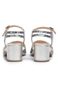 Korkokenkät, joissa on metallinhohtoinen hopeinen lohkokorko, värikkäät hohtavat hihnat ja säädettävä nilkkahihna. Avoin varvasmuotoilu.