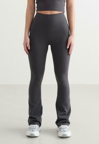 Grijze, aansluitende leggings van rekbare stof, met een hoge tailleband en uitlopende onderkant. Draag ze met grijze sportschoenen.