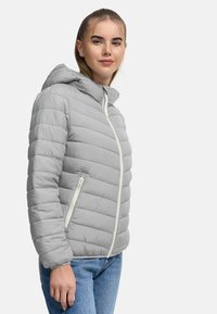 Lichtgrijze gewatteerde jas met een ritssluiting en een kap, met horizontale gestikte lijnen en zijzakken. Draagend over blauwe jeans.