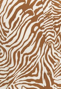 Brun og hvidmønstret skjorte med abstrakte zebra-striber, der har en knapdetalje og et blødt, tekstureret stof.