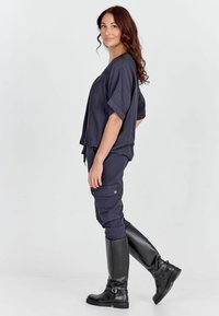 Námornícky modrý krátky top s krátkymi rukávmi, kombinovaný s námorníckymi cargo nohavicami s vreckami a gombíkmi. Čierne čižmy po kolená. Hladká textúra.