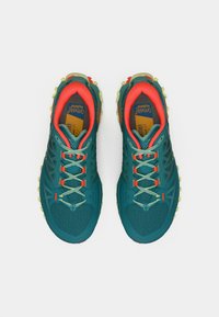 Ténis de corrida em trilhos nas cores teal e laranja, com upper de malha texturizada, detalhes refletivos e tachas amarelas na sola para melhor tração.