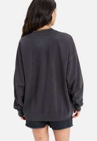 Felpa nera over-size con scollo e polsini a costine, realizzata in morbido cotone. Abbinata a pantaloni shorts in denim nero con orlo sfrangiato.