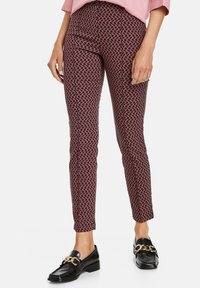 Pantaloni a sigaretta con motivo geometrico rosso e nero, realizzati in un tessuto liscio. Abbinati a mocassini neri.