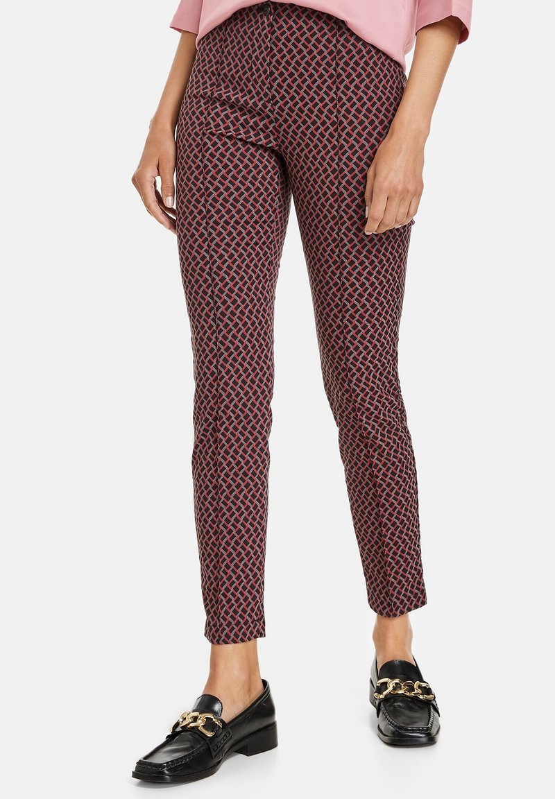 Pantaloni a sigaretta con motivo geometrico rosso e nero, realizzati in un tessuto liscio. Abbinati a mocassini neri.