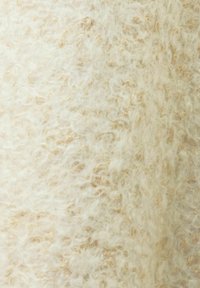 Gros plan sur un tissu en laine couleur crème, doux et moelleux, avec une surface bouclée et texturée et des nuances beige clair.