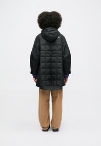 Czarna pikowana kurtka z kapturem, o luźnym kroju i w wzór rombów. Zestawiona z beżowymi, luźnymi spodniami.