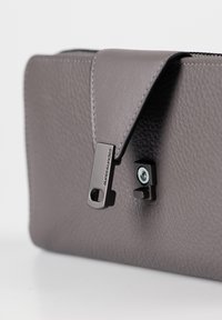 Gray leather bag with smooth texture, featuring a flap closure and black metal hardware accents. Notable zipper pull detail displayed.