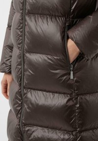 Daunenjacke in Dunkelbraun mit glänzender Textur, horizontal gestepptem Design und einer sichtbaren seitlichen Reißverschlusstasche.