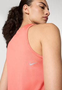 Roza atletska majica bez rukava s mrežastom teksturom, s niskim leđima i malim srebrnim Nike logotipom sa strane.