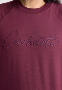 Burgunderfarget genser med myk tekstur og brodert "Carhartt"-logo i en mørkere nyanse, rund halslinning og raglanermer.