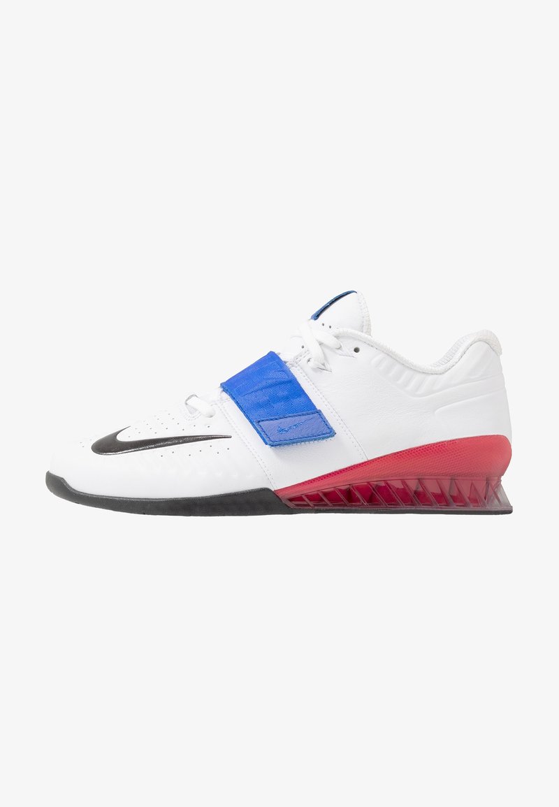 Zapatilla deportiva blanca con suela negra, sección del talón roja, tira ajustable azul y el logo Nike en negro en la zona delantera.