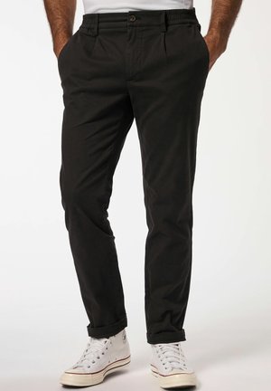 Chinos neri con una vestibilità rilassata, dotati di tasche frontali, chiusura con bottone e orli cuffati, indossati con sneakers bianche. Tessuto dalla texture liscia.