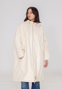 Kremowy, oversize'owy płaszcz z zapięciem na zamek, regulowanym kapturem i bocznymi kieszeniami. Z mankietami oraz gładką teksturą.