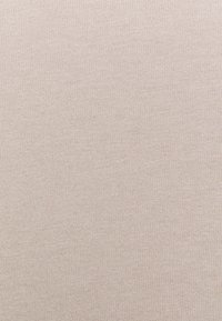 Ljust beige tyg med en fin ribbad textur, som visar en mjuk, stickad design, jämn färg med minimala variationer.