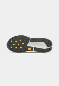 Semelle en caoutchouc noir avec des accents jaunes, présentant un motif de semelle en forme de flèches. La semelle intermédiaire est grise avec un design texturé. Logo Vibram présent.