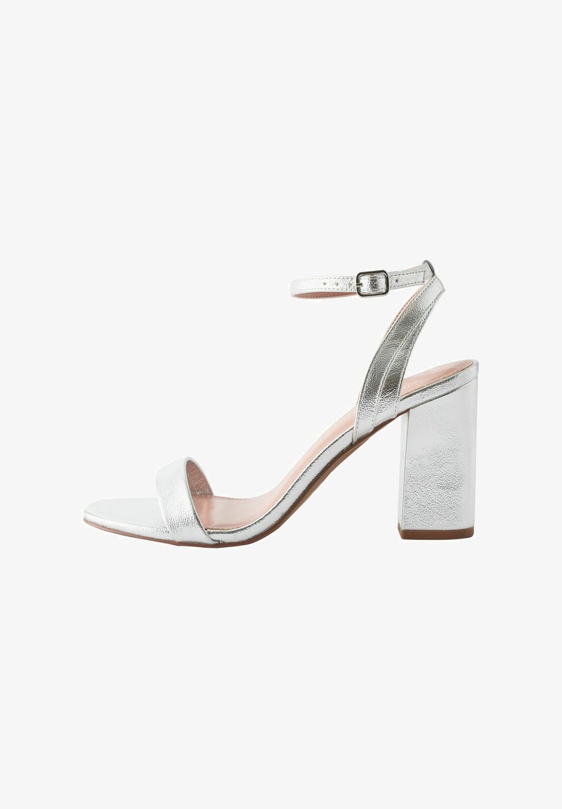 Silver metallisk högklackad sandal med justerbart ankelsnöre, öppen tå och bred blockklack. Slät yta med minimalistisk design.